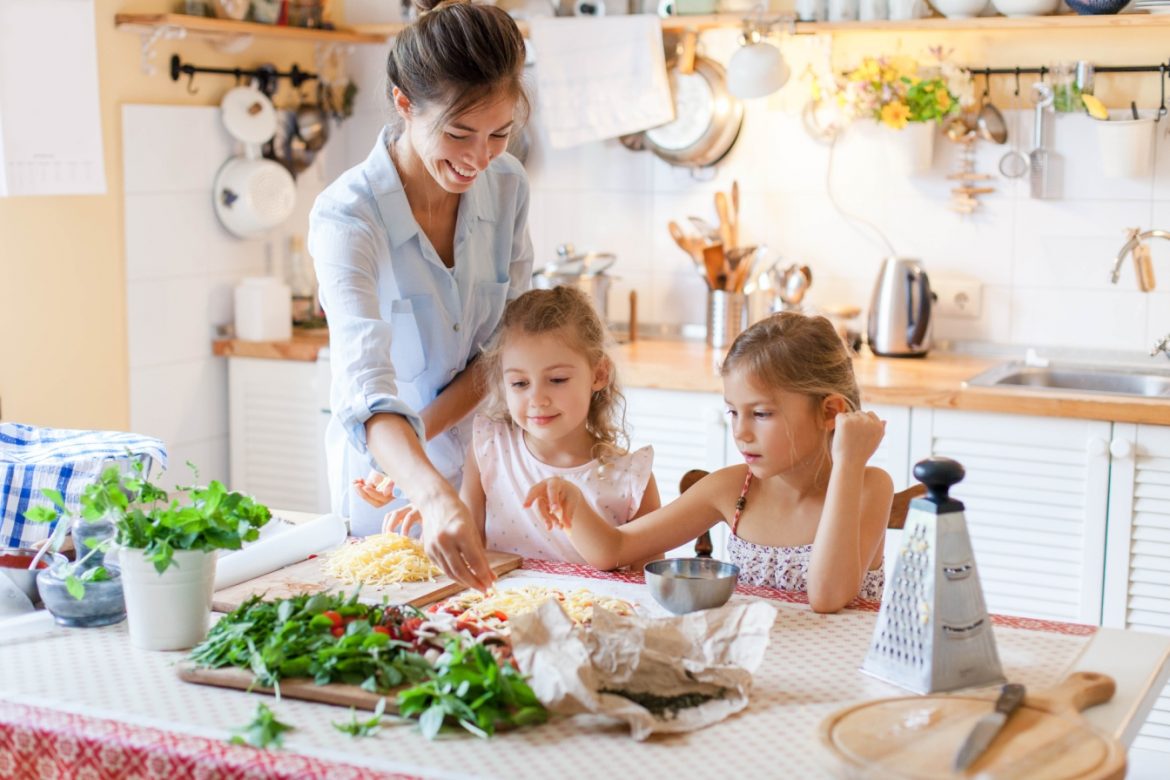 Fleksitarianizm - jak ograniczyć spożycie mięsa w diecie? Mama wraz z dwiema córkami przygotowują obiad w kuchni.