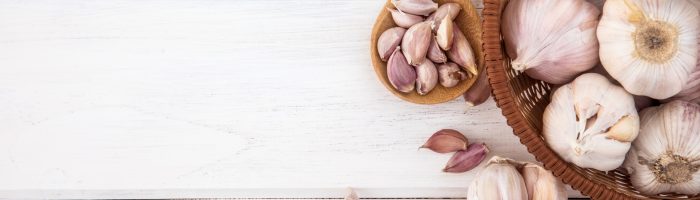 7 produktów, które wzmacniają jelita. Probiotyki i prebiotyki: czosnek, jogurt, cykoria, kombucha, szparagi, cebula, kiszonki. Główki czosnku w koszyczku na białym drewnianym stole.