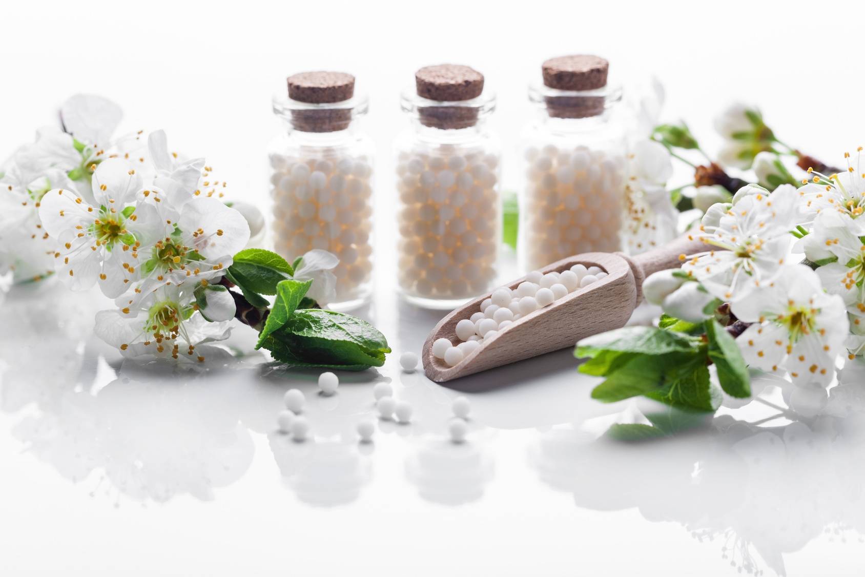 Ignatia amara - lek homeopatyczny w 3 fiolkach stoi na białym blacie obok białych kwiatów jabłoni.