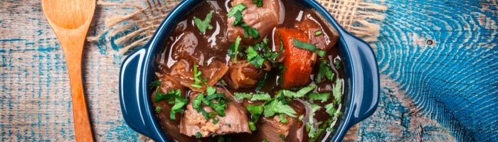 Dieta lekkostrawna - przepisy na zupy lekkostrawne i lekkostrawny obiad. Duszona potrawka z chudego mięsa w niebieskiej miseczce żaroodpornej, obok leży drewniana łyżka.