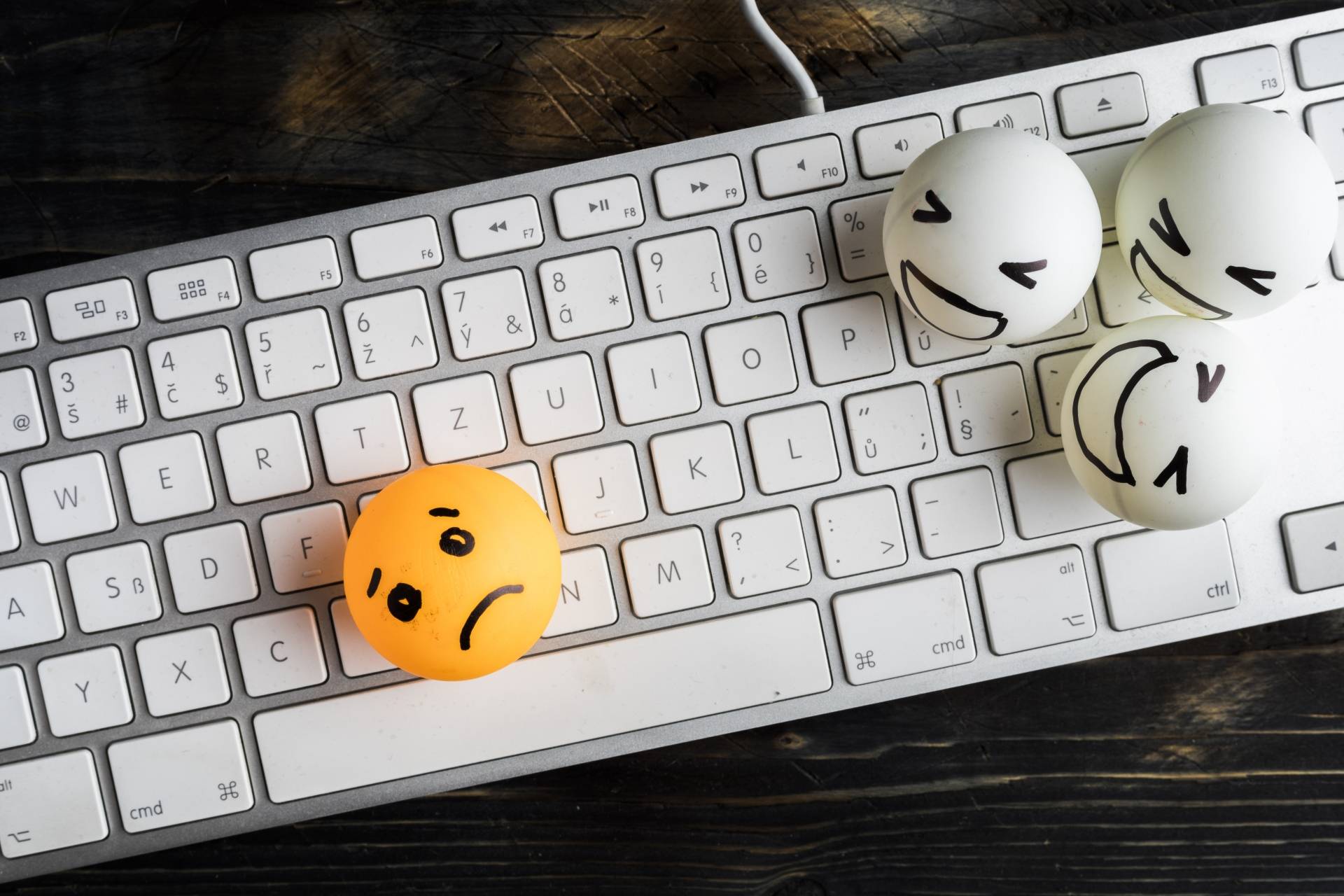 Hejt w sieci - jak mu zaradzić? Na klawiaturze komputera leżą piłeczki do ping ponga z narysowanymi buźkami - 3 hejterów vs ofiara.