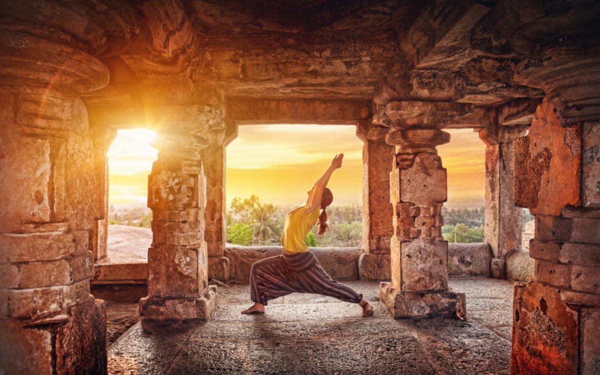 Historia jogi - jak powstała joga? Kobieta w asanie w środku starożytnej świątyni w Indiach.