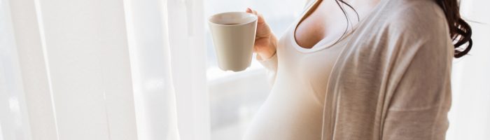 Leki homeopatyczne na dolegliwości w ciąży. Kobieta ciężarna pije herbatę z kubka, wyglądając za okno.