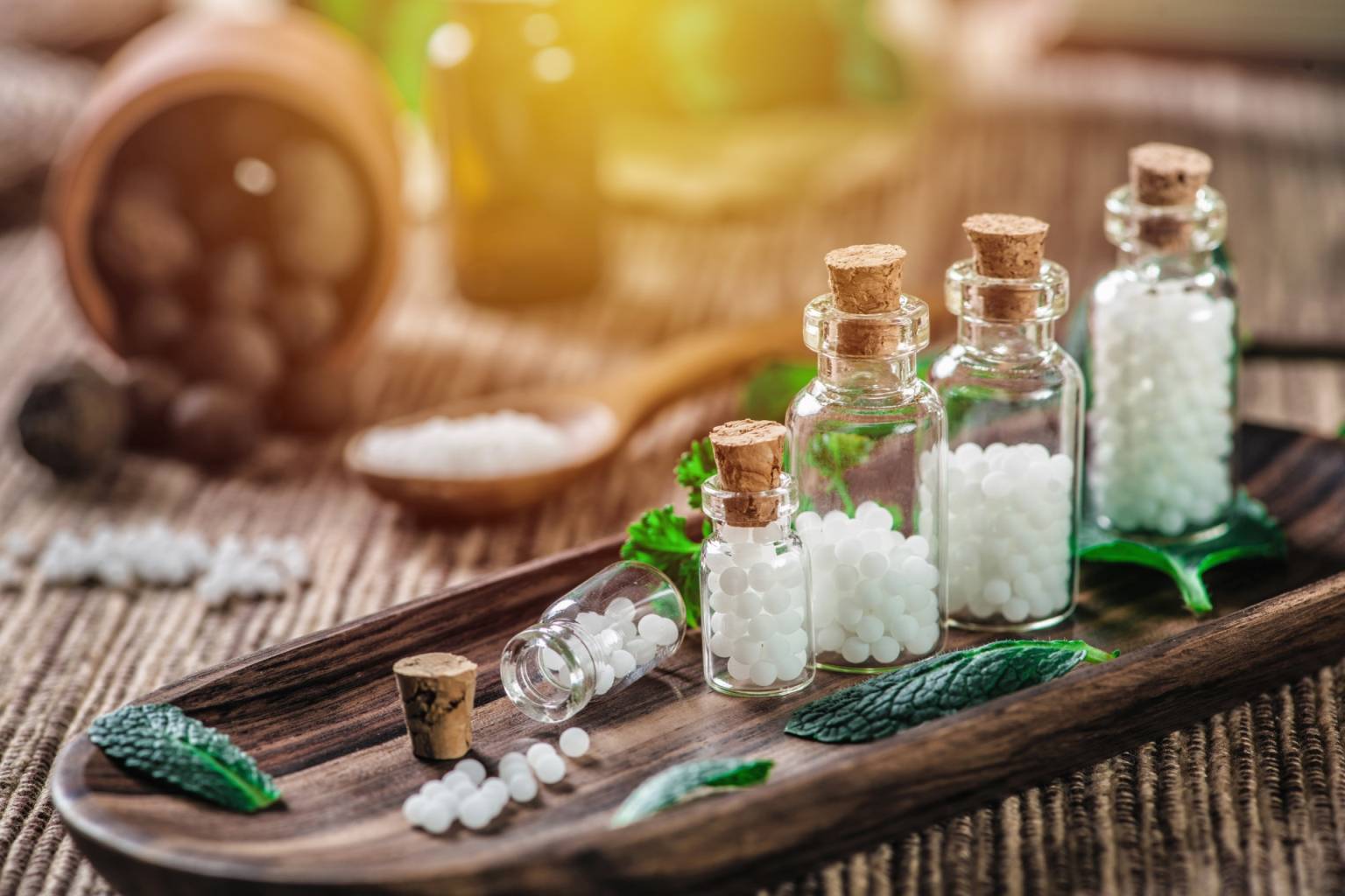 Leki homeopatyczne w buteleczkach stoją na drewnianym półmisku. Homeopatia na stłuczenia i ból po urazie.