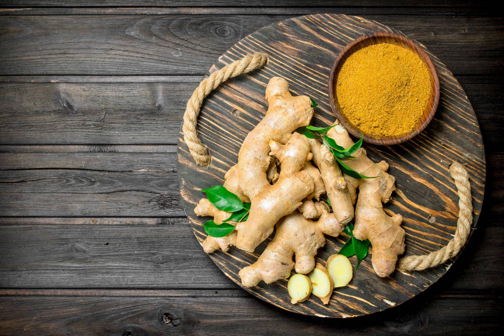 Imbir - dlaczego warto go jeść? Kłącza imbiru i sproszkowany imbir w miseczce na drewnianej desce.