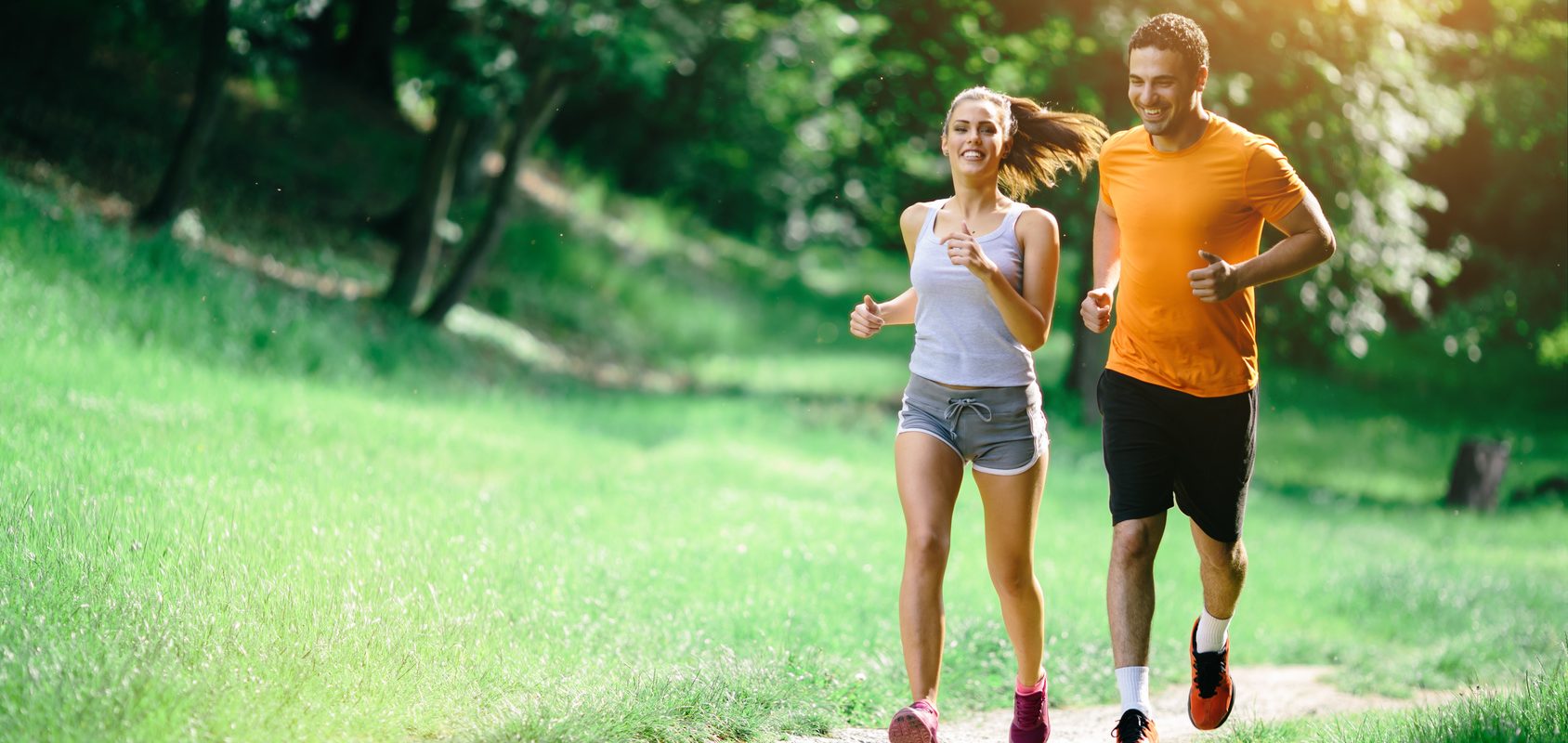 Bieganie w upale - jak bezpiecznie biegać w upalne dni? Kobieta i mężczyzna uprawiają jogging w parku latem.