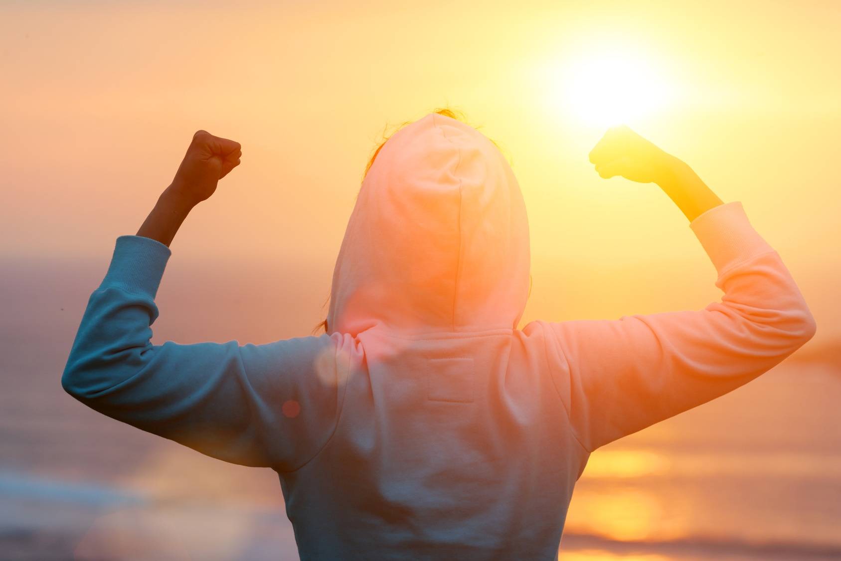 Jak wygrać z otyłością? Kobieta w bluzie z kapturem skończyła jogging o zachodzie słońca nad morzem.