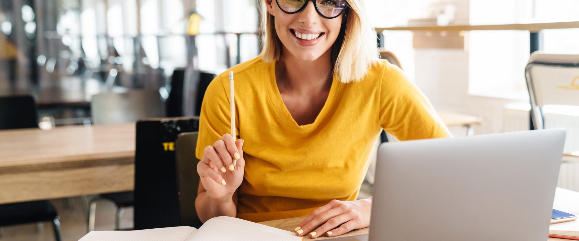 Iloraz inteligencji - czy jesteśmy w stanie zwiększyć swoje IQ? Uśmiechnięta kobieta w okularach i żółtym swetrze siedzi przed laptopem.