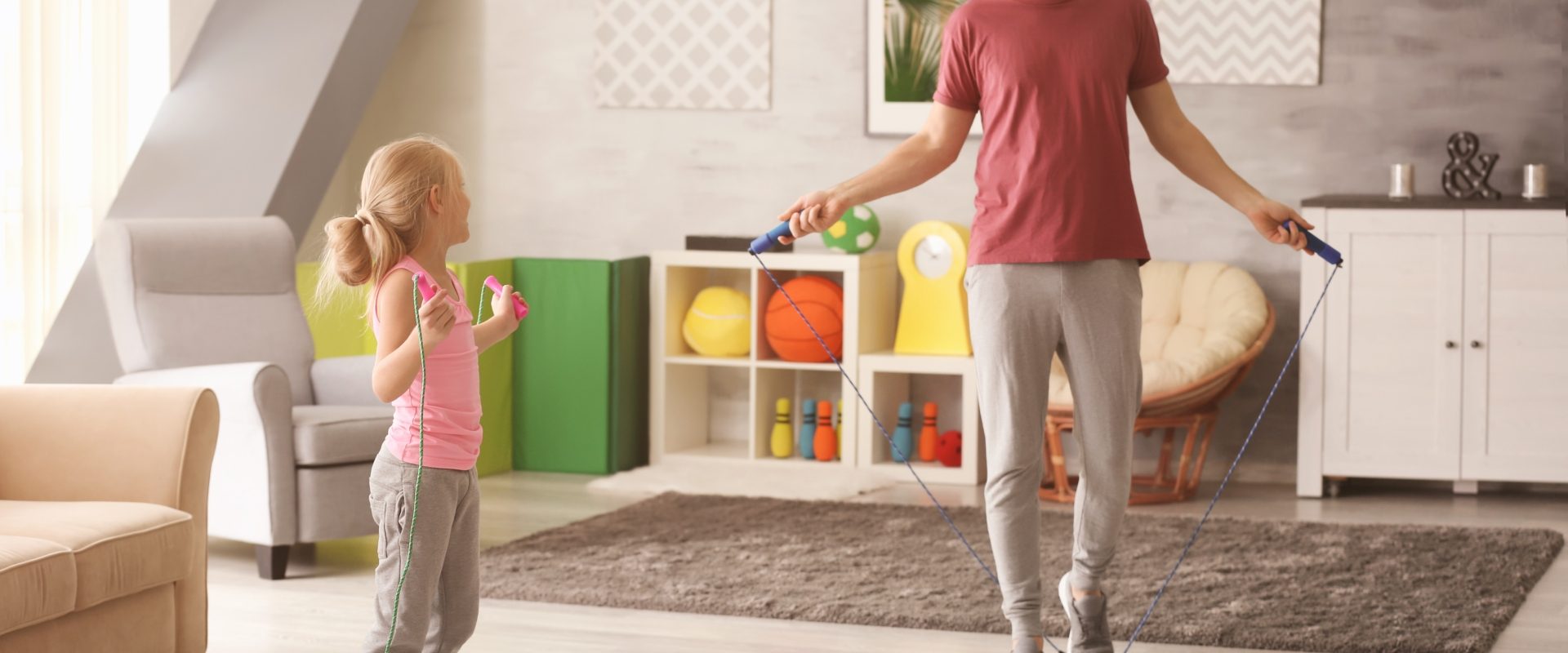 Jak ćwiczyć z dziećmi? Ojciec z córką trenują ze skakanką w domu.