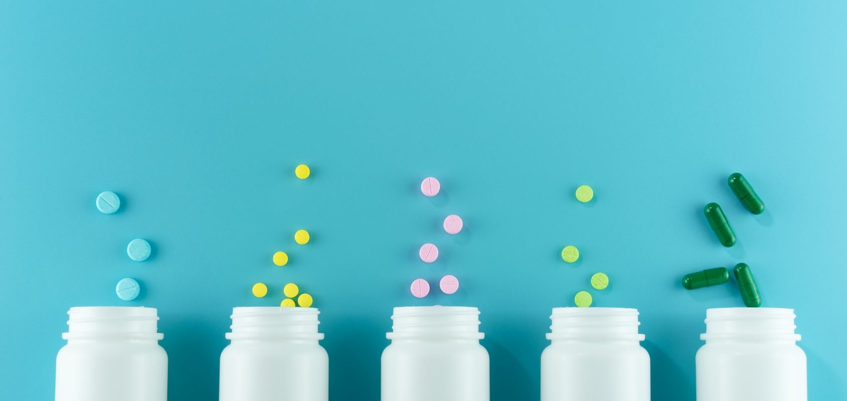 Jak działają leki i jak przyjmować leki, aby były dla nas bezpieczne? Jak uniknąć interakcji pomiędzy lekami oraz lekami a żywnością? Białe opakowania leków na niebieskim tle.