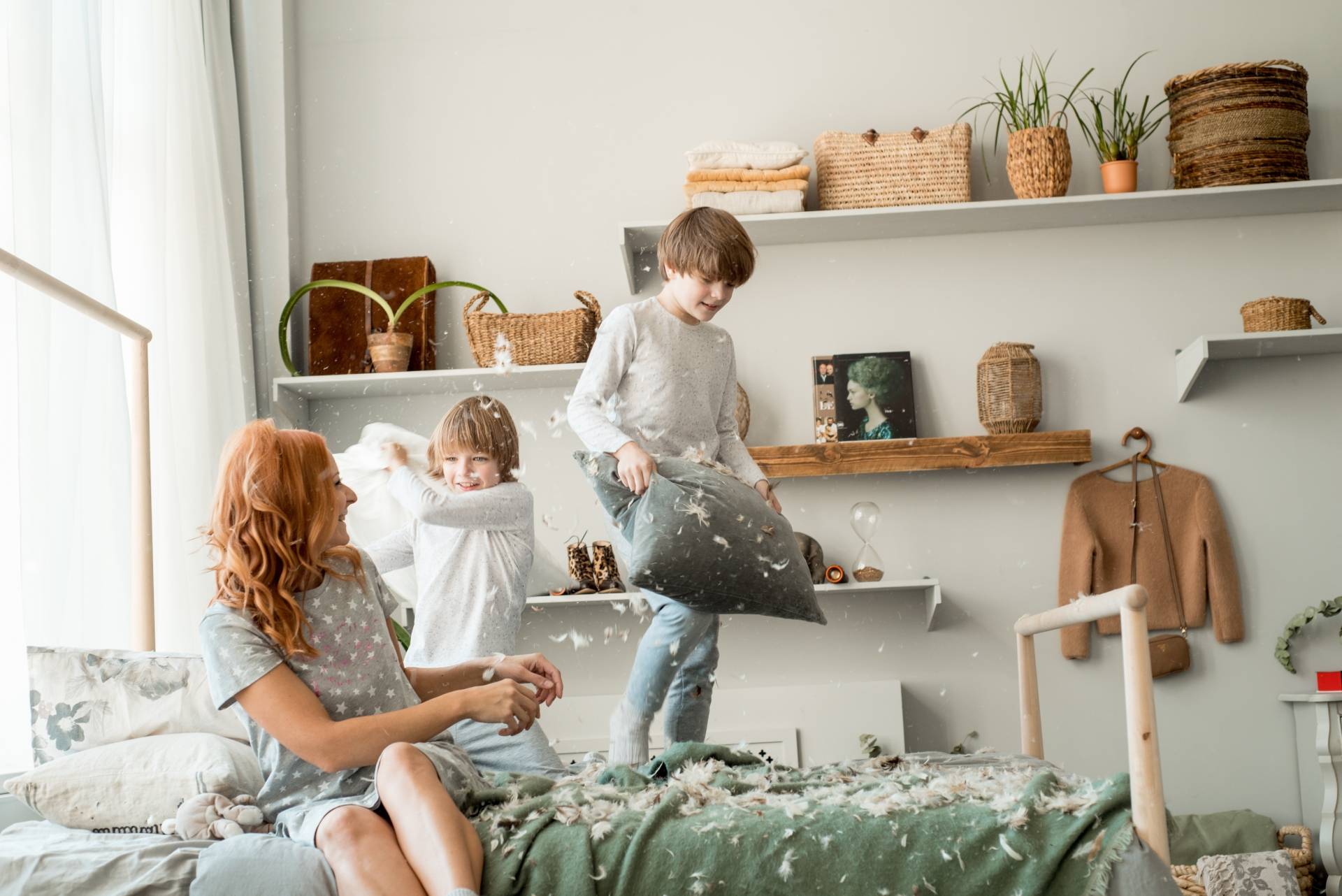 Jak rozwiązywać konflikty między rodzeństwem? Mama siedzi na łóżku i godzi skłóconych braci, którzy walczyli na poduszki.