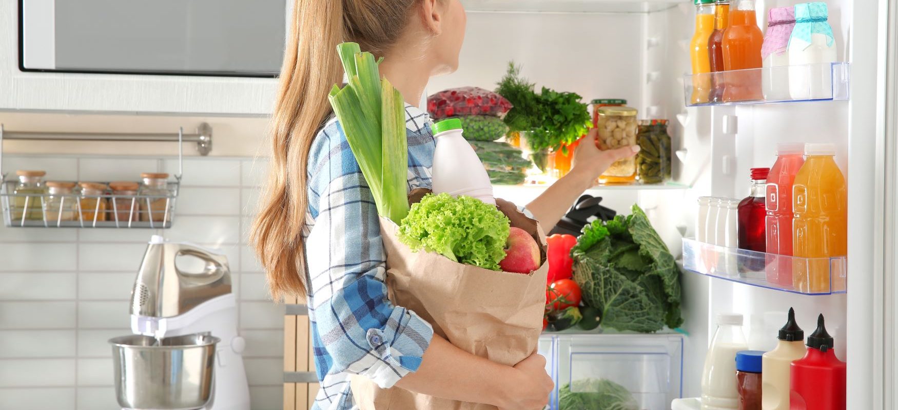 Jak nie marnować jedzenia? Nurt zero waste w kuchni. Kobieta wkłada zakupy do lodówki.