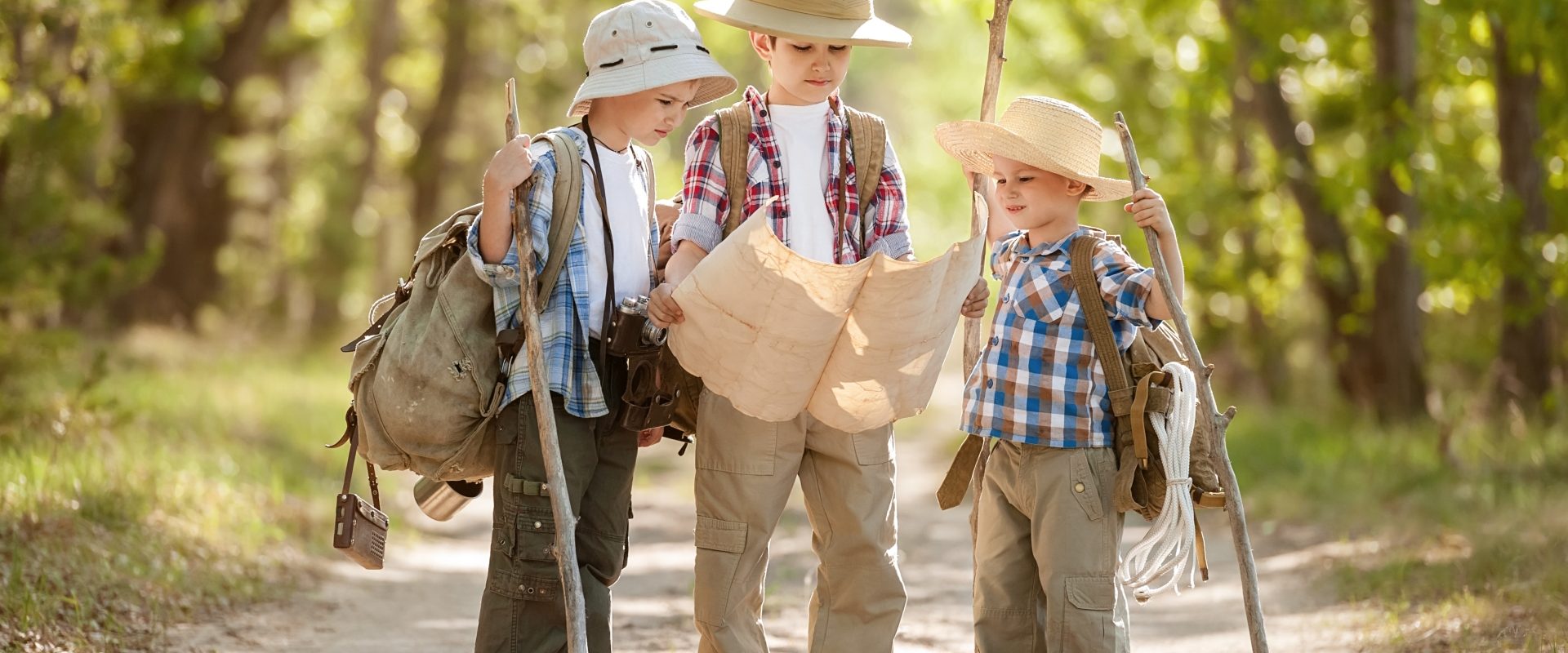 Jak nie zgubić się w lesie opowiada Adam Wajrak. Trzech małych chłopców ubranych jak podróżnicy patrzy na mapę i szuka drogi w lesie.