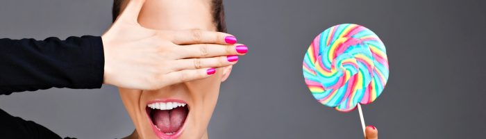 Jakie są objawy cukrzycy typu 2, jak ją rozpoznać? Kobieta w czarnym golfie w jednej ręce trzyma kolorowego lizaka, drugą ręką zasłania sobie oczy.