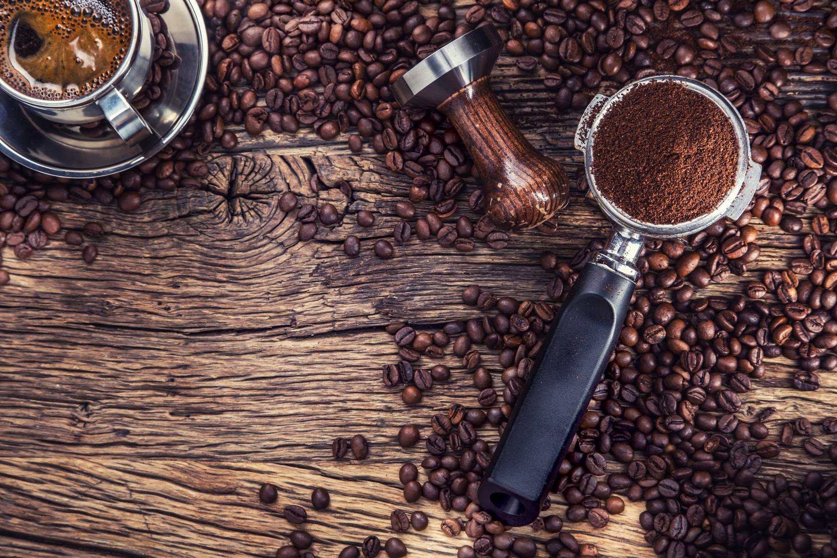 Jak parzyć kawę według zasad diety pięciu przemian? Ziarna kawy rozsypane na drewnianym stole, obok stoi filiżanka czarnej kawy i kawa już zmielona.