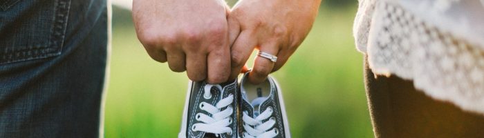 Niepłodność w ujęciu medycyny chińskiej. Kobieta i mężczyzna stoją na łące i trzymają w rękach małe trampki dla dziecka.