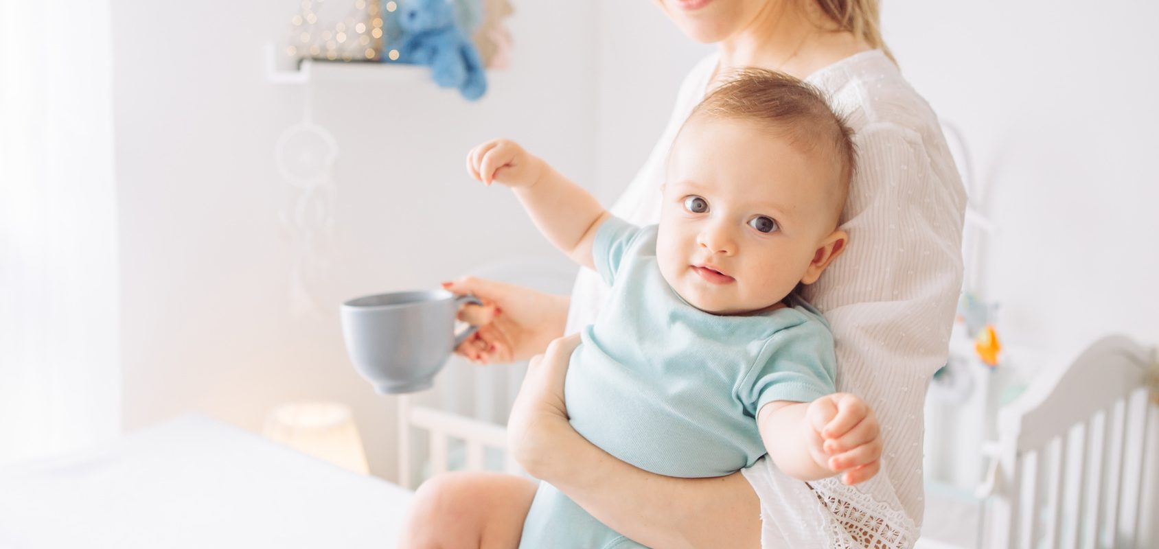 Ból pleców po porodzie - jak zadbać o kręgosłup młodej mamy? Kobieta nosi niemowlę na rękach.