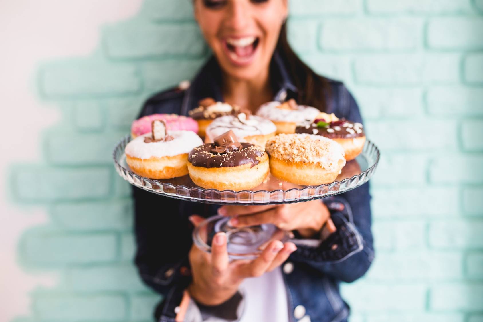 Uzależnienie od słodyczy - jak z nim walczyć? Jak ograniczyć słodycze? Jak zmniejszyć apetyt na słodycze? Uśmiechnięta dziewczyna trzyma w rękach paterę z lukrowanymi pączkami.