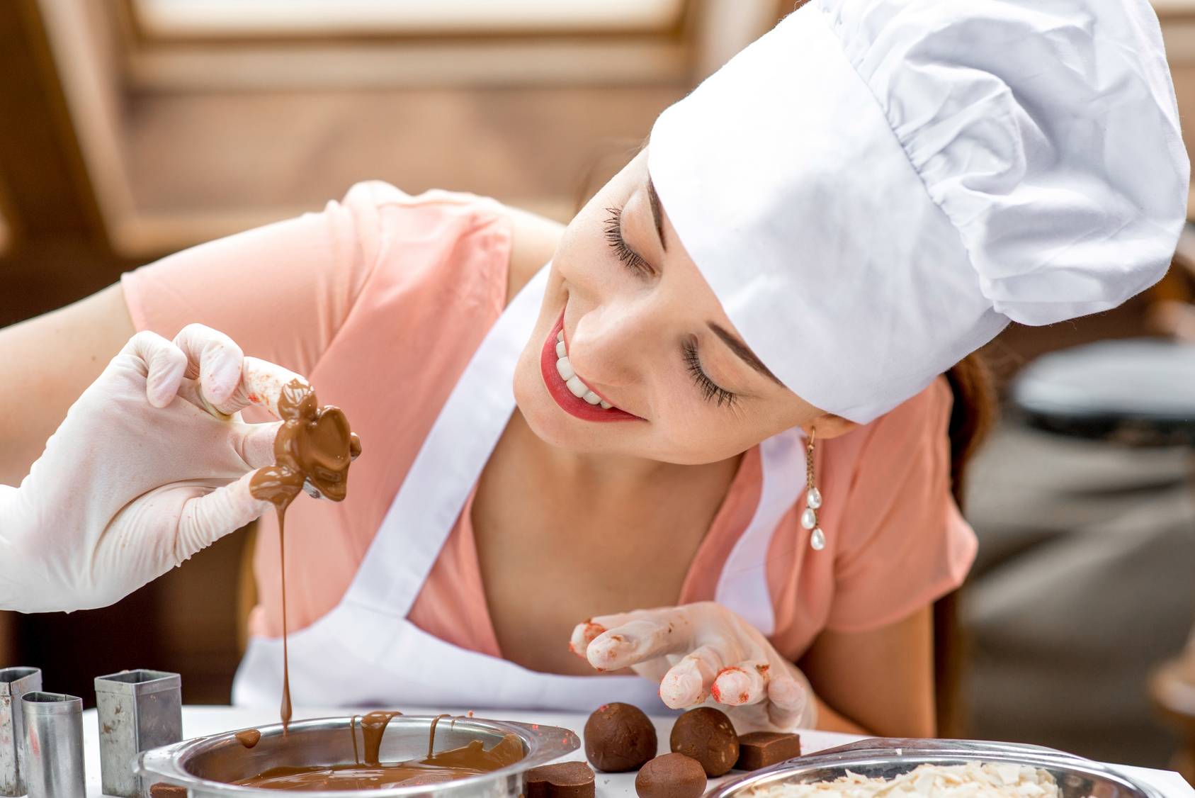 Jak powstaje czekolada? Kobieta cukiernik przygotowuje czekoladowe pralinki.