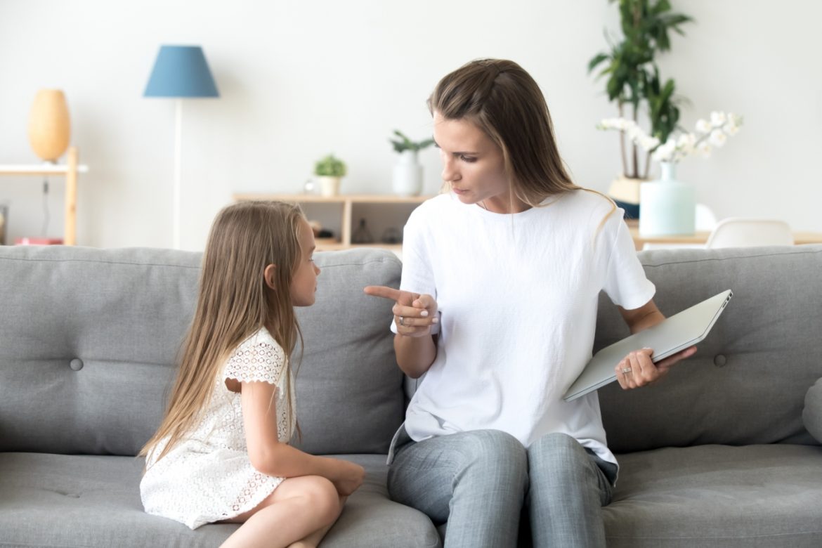 Jak reagować na złość u dziecka? Mama poucza córeczkę, jak powinna się zachowywać, obie siedzą na szarej kanapie w domowym salonie.