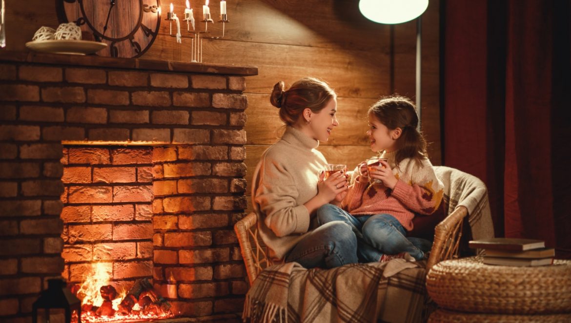 5 sposobów na wzmocnienie śluzówki nosa i jamy ustnej. Mama z córką siedzą wieczorem w fotelu przy kominku i piją herbatę w przytulnym salonie.