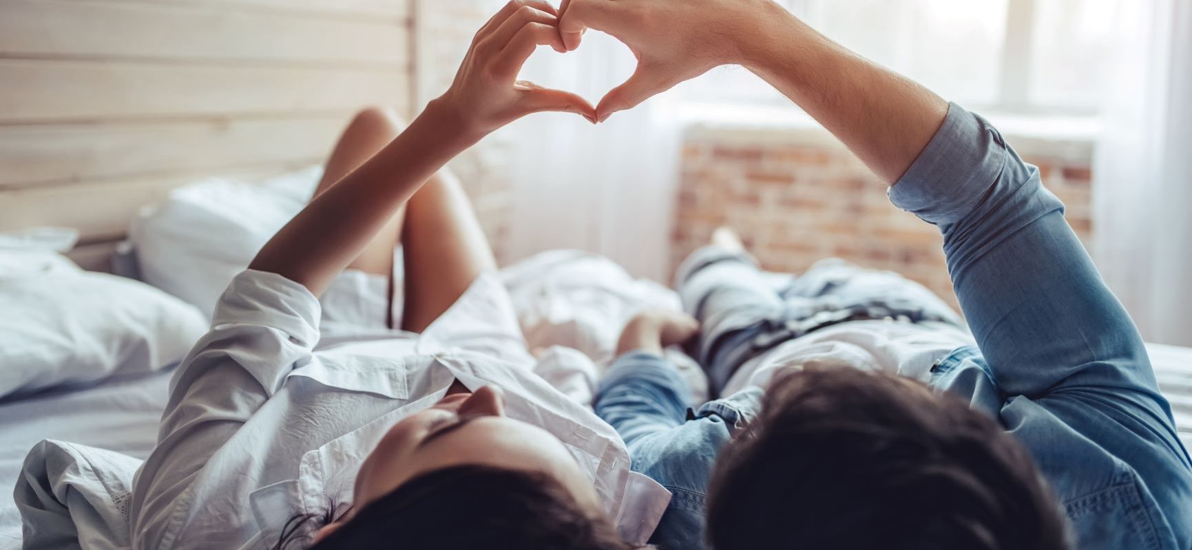 Jak często uprawiać seks, aby zajść w ciążę? Zakochana para leży na łóżku w sypialni i układa swoje dłonie w kształt serca.