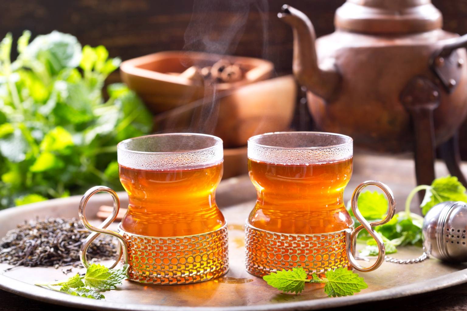 Czarna herbata w szklankach z osłonką na metalowej tacy, w tle stoi imbryk.