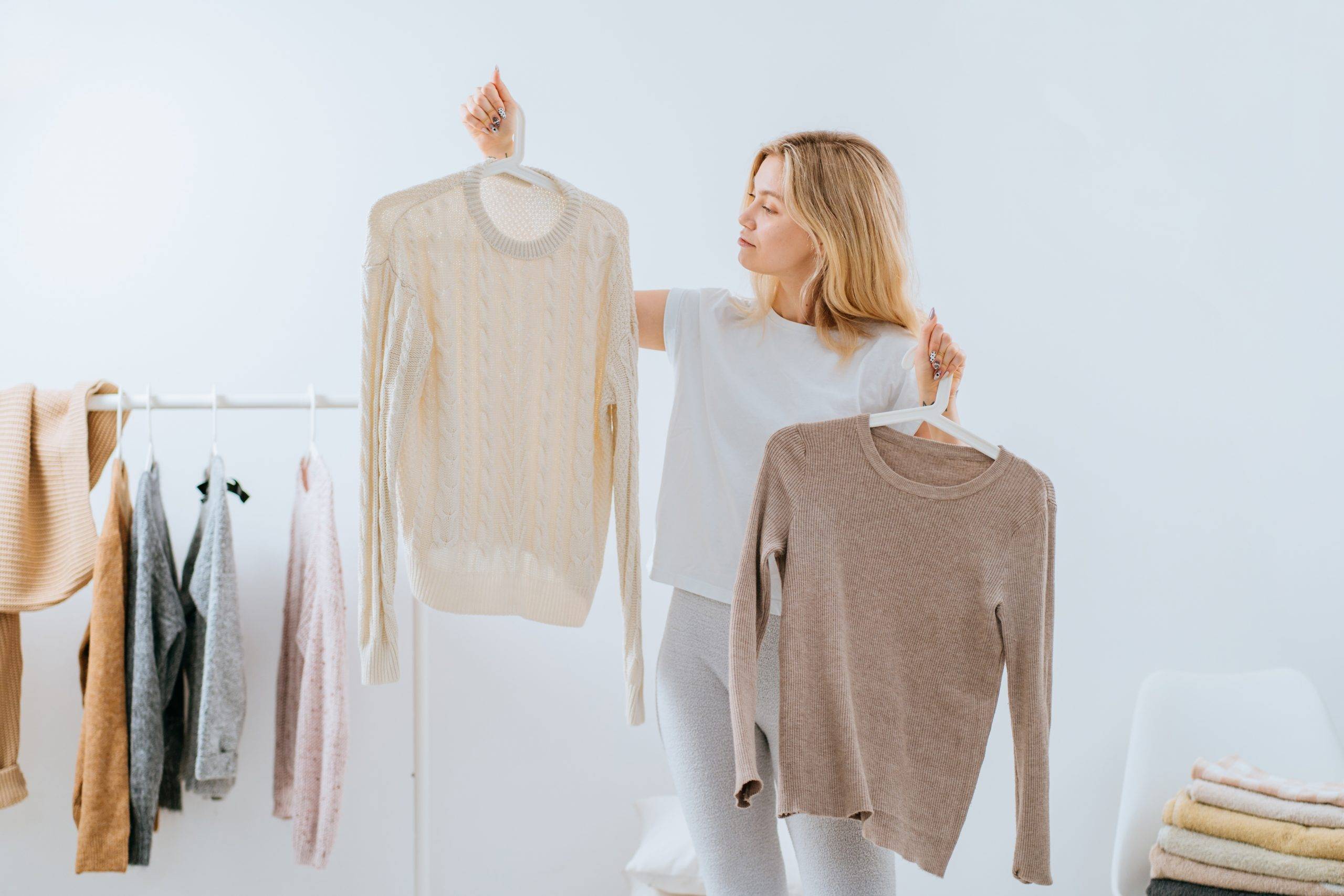 Minimalizm w szafie - jak zrobić porządki w ubraniach? Gdzie oddać ciuchy, których już nie nosimy? Kobieta przegląda swetry, w których rzadko chodzi.