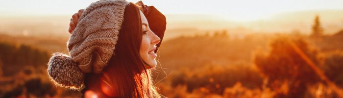 Przyczyny chorób według medycyny chińskiej. Jakie czynniki zewnętrzne odpowiadają za choroby? Dziewczyna w wełnianej czapce z pomponem podziwia wiejski krajobraz o zachodzie słońca.