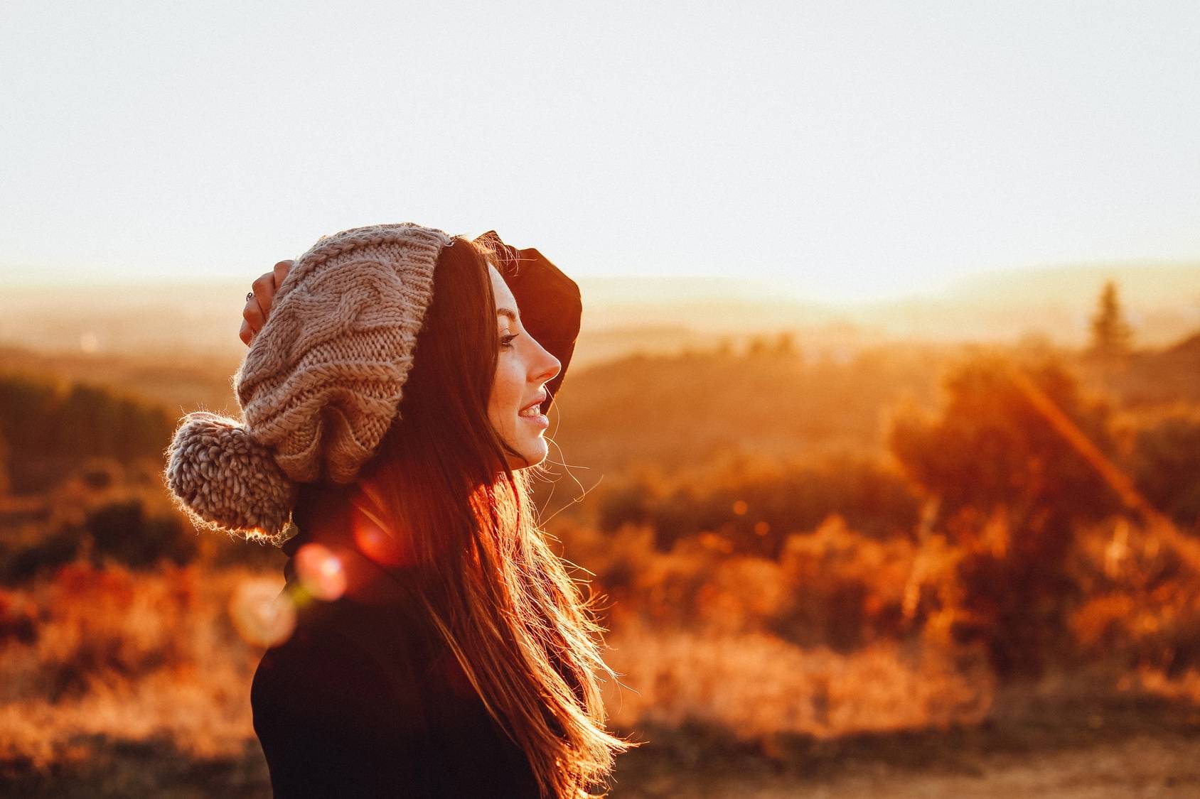 Przyczyny chorób według medycyny chińskiej. Jakie czynniki zewnętrzne odpowiadają za choroby? Dziewczyna w wełnianej czapce z pomponem podziwia wiejski krajobraz o zachodzie słońca.