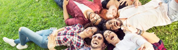 Joga śmiechu - na czym polega śmiechoterapia, czyli terapia śmiechem i czym jest gelatologia? Grupa młodych ludzi śmieje się, leżąc obok siebie w kółku na trawie.