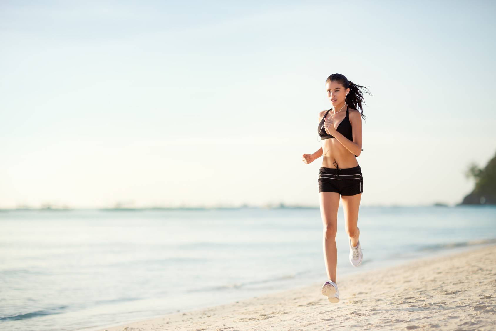 Kremy z filtrem przeciwsłonecznym. Kobieta biega po plaży w stroju sportowym.