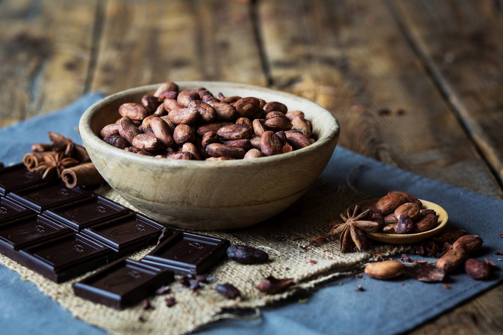 Gorzka czekolada zawiera 90% kakao. ziarna kakaowca w drewnianej miseczce, kawałki tabliczki czekolady.