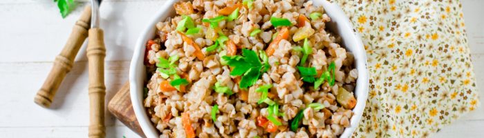 Dieta przy Hashimoto - co jeść przy chorobie tarczycy? Miska kaszy z natką na stole, obok leżą sztućce i ściereczka.