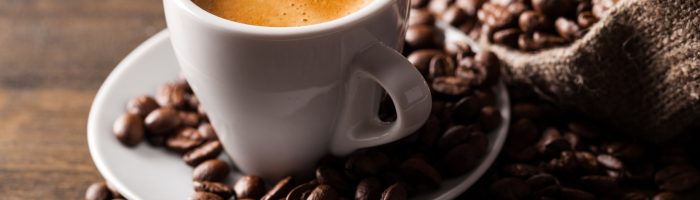 Kawa według diety pięciu przemian. Jakie jest przepis na kawę wg 5 przemian? Świeżo zaparzona kawa espresso w białej filiżance, obok leżą ziarenka kawy.