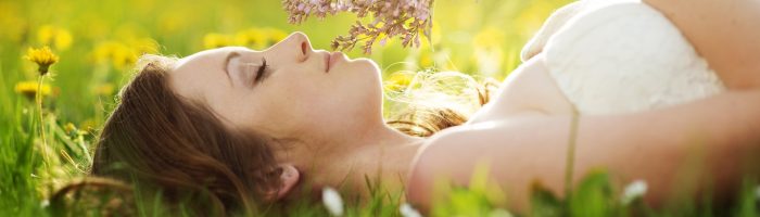 Kiedy i jak zbierać zioła? Młoda kobieta leży na trawie, trzymając w dłoni bukiet ziół.