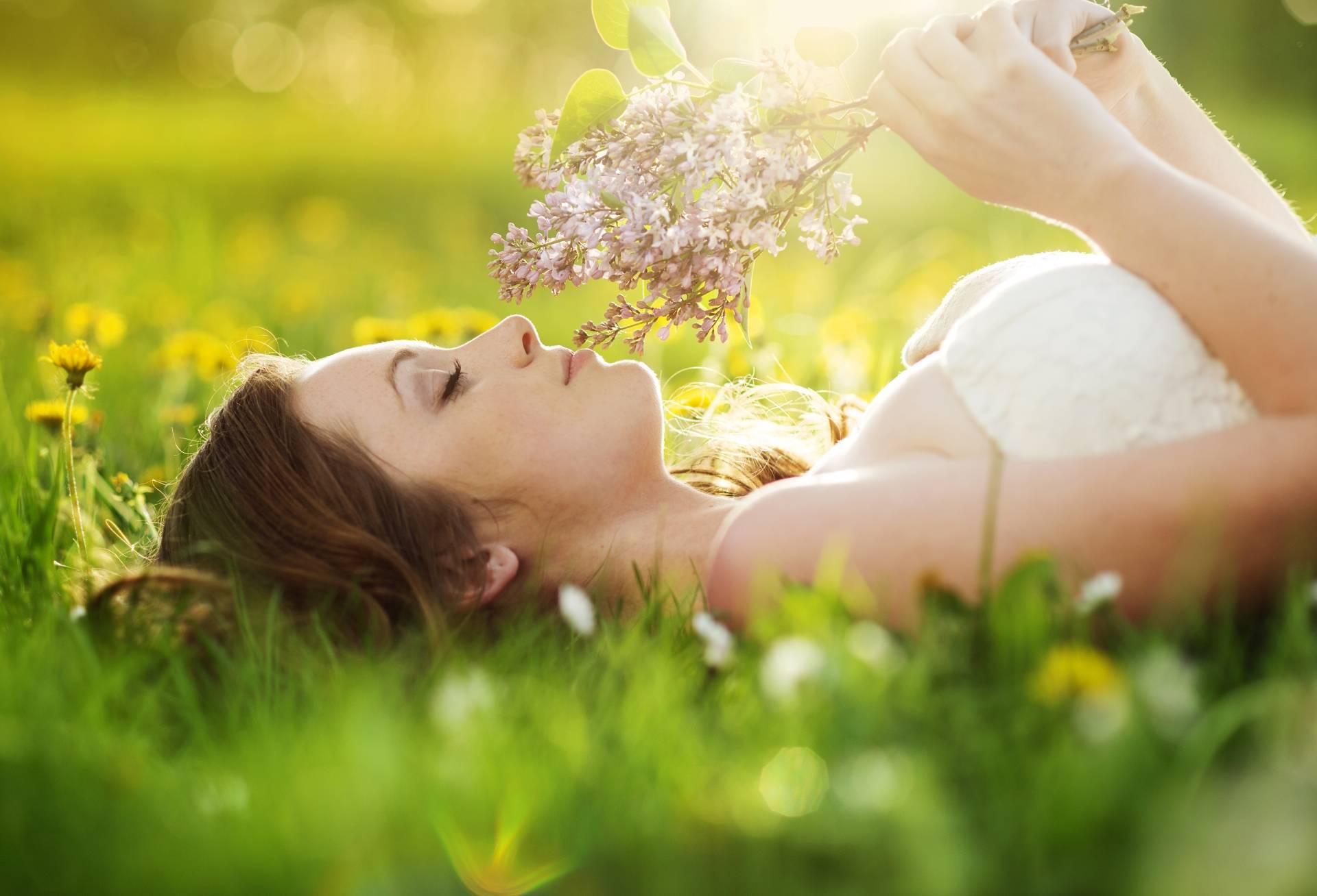 Kiedy i jak zbierać zioła? Młoda kobieta leży na trawie, trzymając w dłoni bukiet ziół.