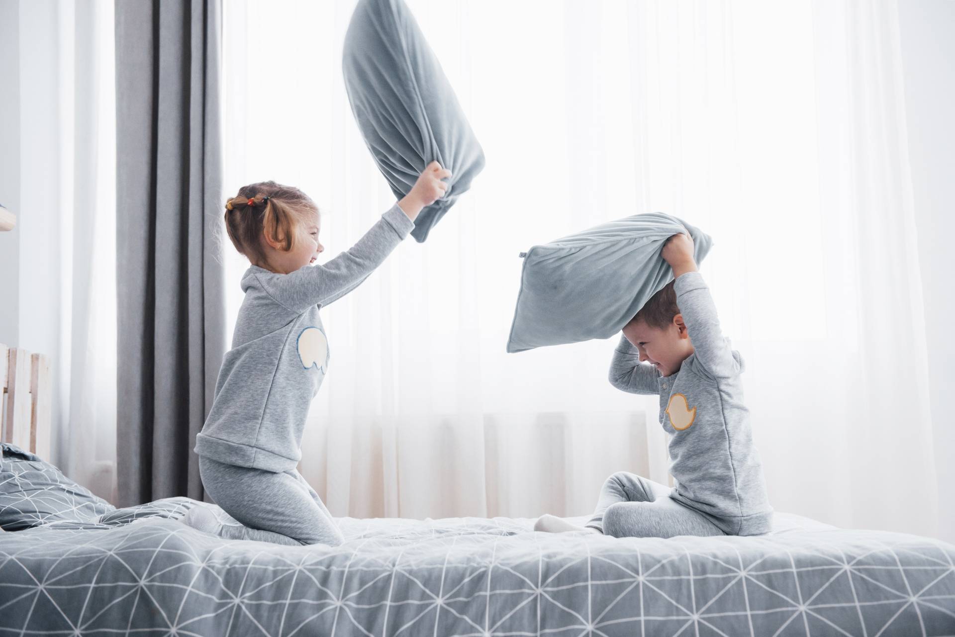 Kłótnie i wojny między rodzeństwem - jak im zapobiegać? Dzieci w piżamach biją się na poduszki na łóżku.