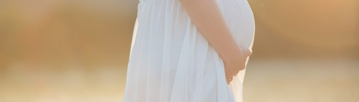 Jak dbać o siebie w ciąży według tradycyjnej medycyny chińskiej? Kobieta w ciąży w białej sukience boho spaceruje po łące.