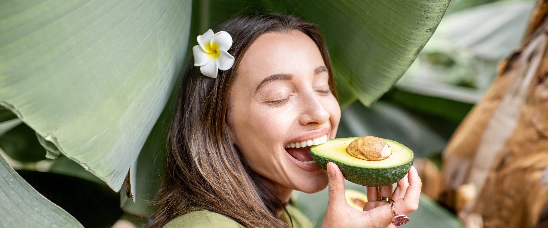 Ciemna strona awokado - jak kartele narkotykowe wyzyskują rolników w Meksyku i wycinają lasy deszczowe. Kobieta je awokado stojąc na tle liści bananowca.