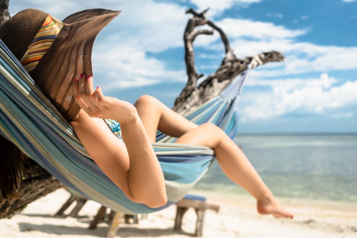 Filtry przeciwsłoneczne - jak wybrać bezpieczne? Kobieta na wakacjach opala się w hamaku na plaży.
