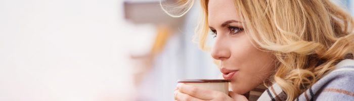 Jak zadbać o chore zatoki? Kobieta ubrana w ciepły sweter pije herbatę opierając się balustradę tarasu.