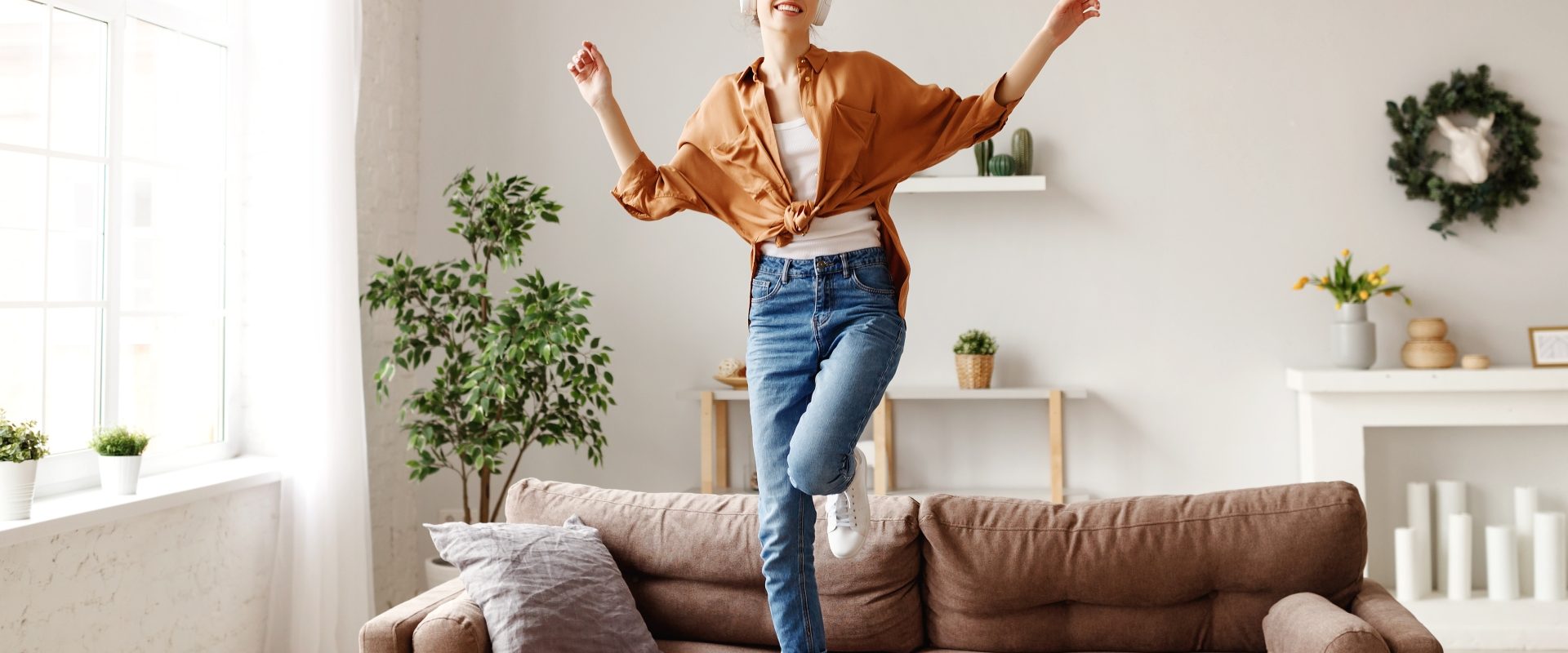 Niedobór żelaza - jakie są objawy i przyczyny, jak leczyć? Szczęśliwa kobieta skacze po kanapie, słuchając muzyki w słuchawkach.