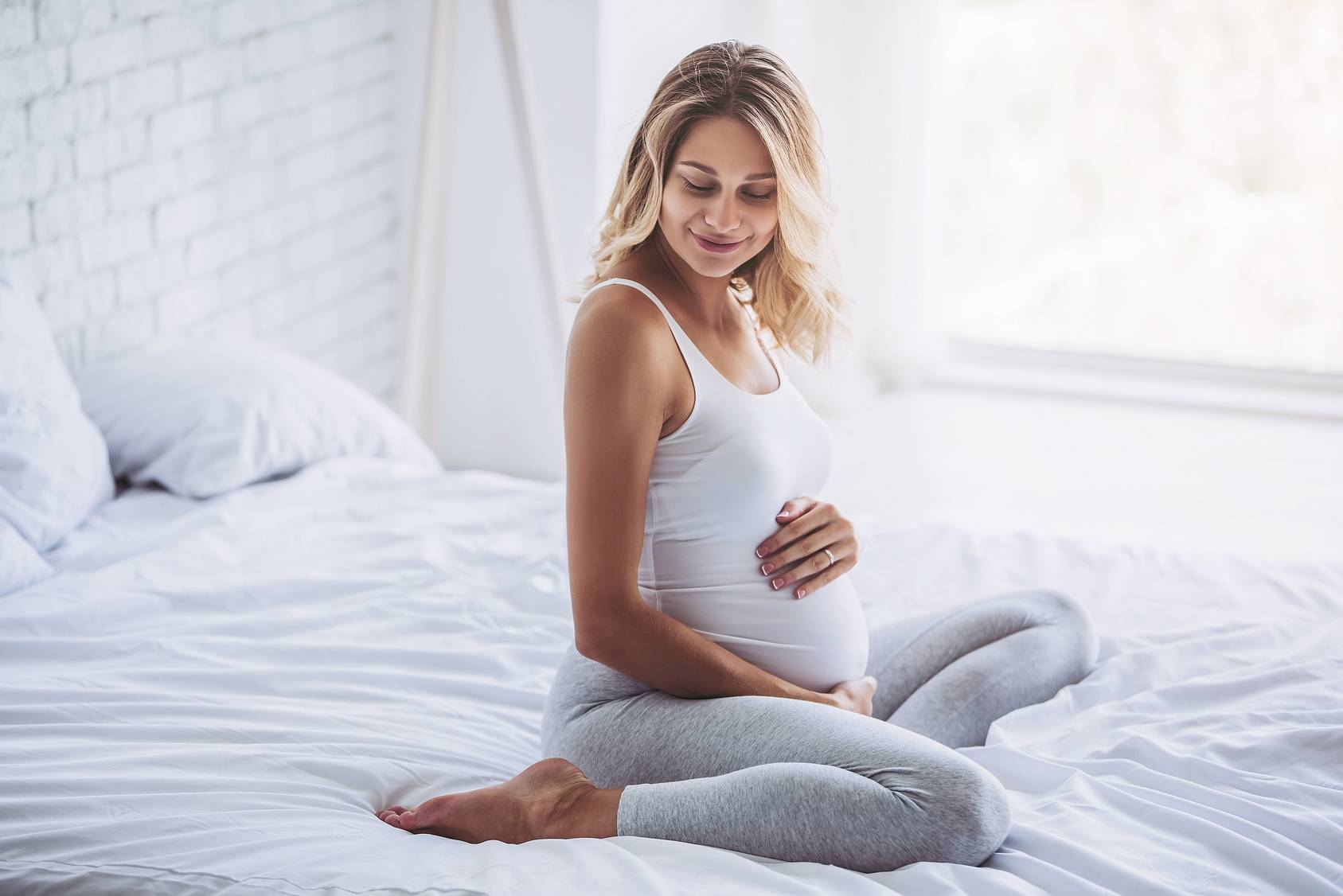 Ciąża po 40. - jak urodzić zdrowe dziecko po 40. roku życia? Kobieta w zaawansowanej ciąży siedzi na łóżku.