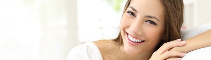 Witamina B12 - sprawdź, czy grozi ci jej niedobór. Jakie są objawy niedoboru witaminy B12? Kobieta siedzi na kanapie w salonie i uśmiecha się do aparatu.