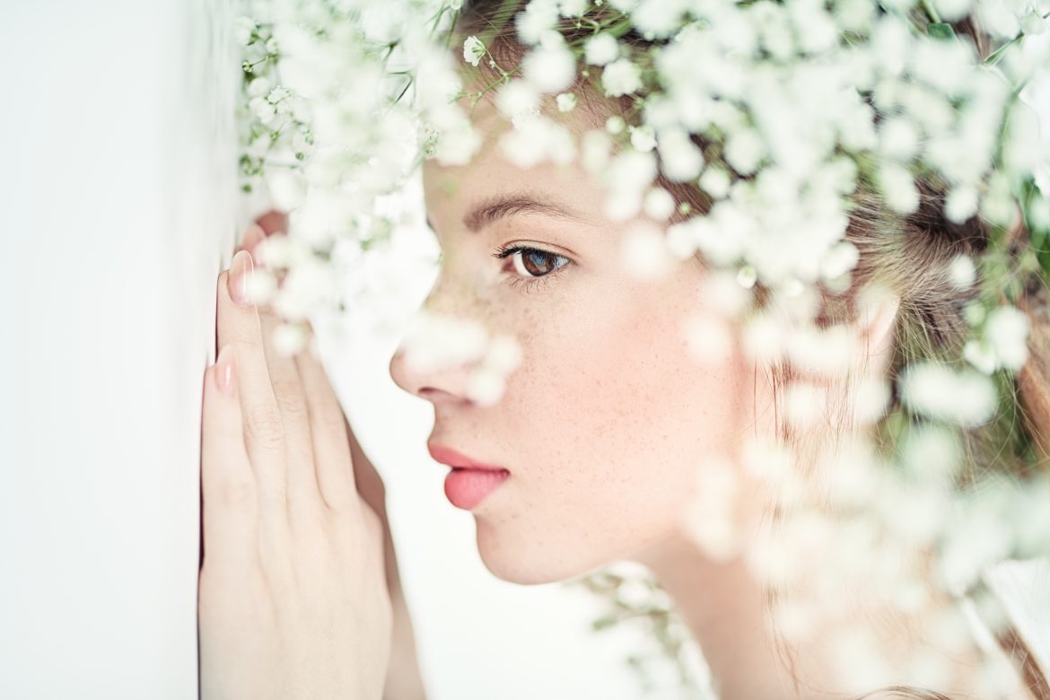 Kwasy na twarz – jak zrobić w domu peeling kwasowy? Dziewczyna o idealnej jasnej cerze w otoczeniu białych kwiatków.