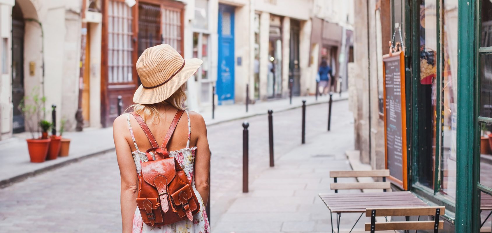 Jak poradzić sobie w mieście w trakcie upałów? Jak przetrwać upały? Kobieta w letniej sukience, kapeluszu słomkowym i plecaku spaceruje po mieście.