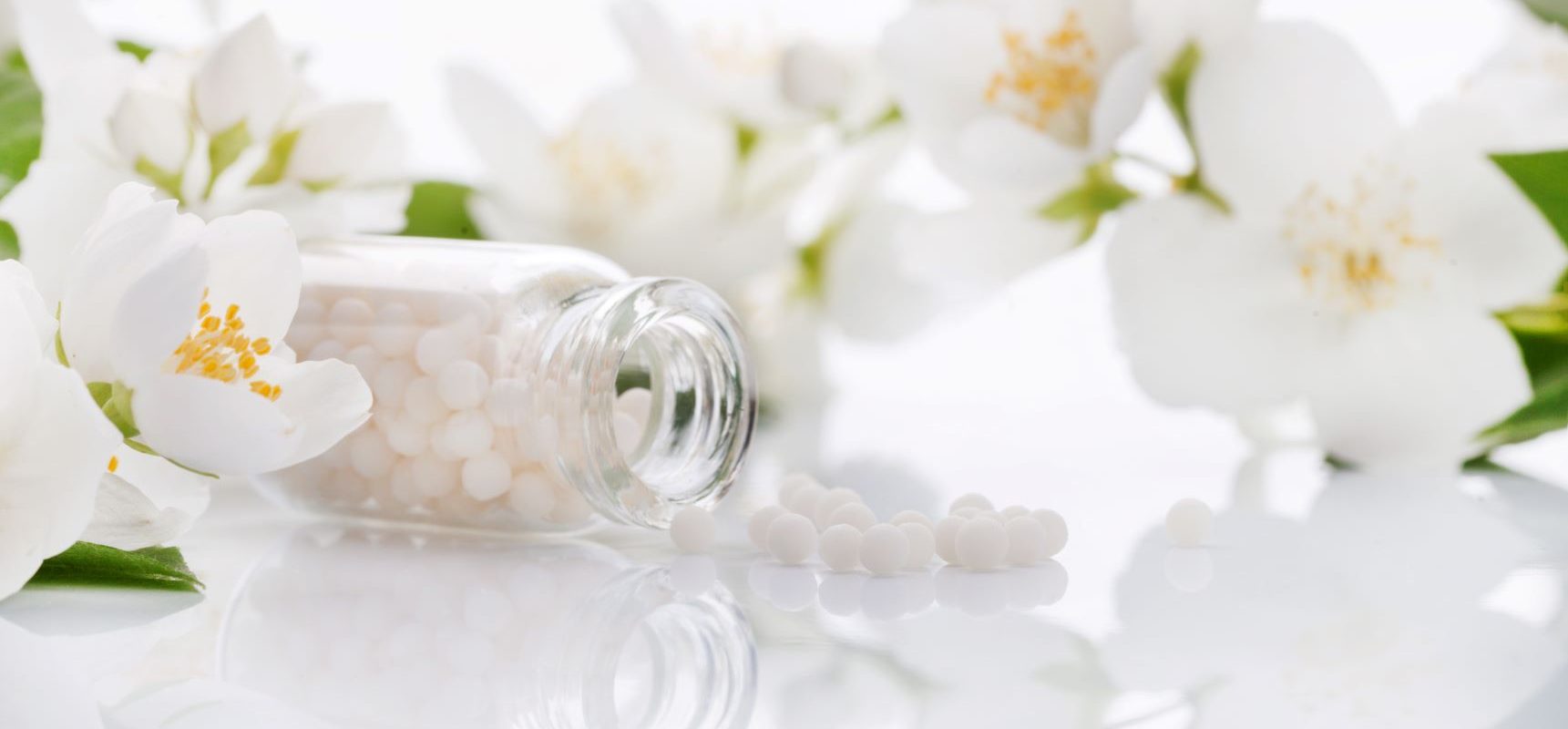 Naturalne sposoby na zatrucie pokarmowe. Jak szybko wyleczyć zatrucie domowymi sposobami i homeopatią? Leki homeopatyczne w fiolce i białe kwiaty jabłoni.