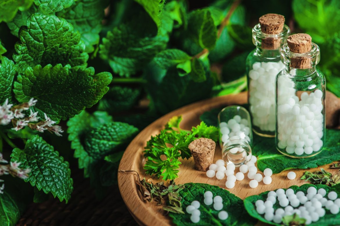 Calcarea phosphorica – lek homeopatyczny na zmęczenie. Homeopatia na dolegliwości w każdym wieku. Leki homeopatyczne w słoiczkach na drewnianej desce w otoczeniu zieleni.