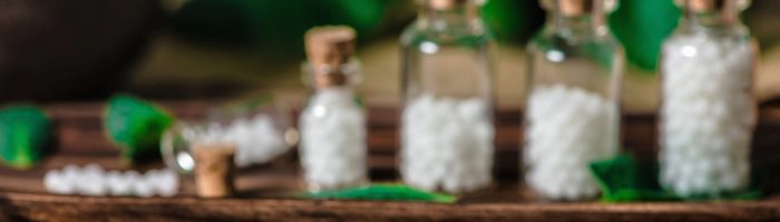 Nux vomica - lek homeopatyczny na niestrawność, wymioty i inne dolegliwości. Fiolki z granulkami homeopatycznymi stoją na drewnianej tacy na drewnianym stole.